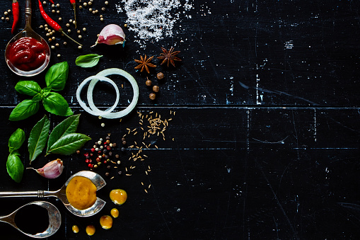 Different type of sauces, fresh herbs and spices on dark vintage background with space for text. Vegetarian food, health or cooking concept.