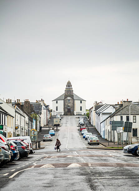 Bowmore, Islay Bowmore, UK - May 5, 2014: Pedestrians on the main road through Bowmore on the isle of Islay off the west coast of Scotland. At the top of the road is the Round Church built in 1767 and designed so that the Devil would have no corner to hide in. Bowmore is the administrative captial of Islay and is probably best known for the Bowmore Distillery. bowmore whisky stock pictures, royalty-free photos & images