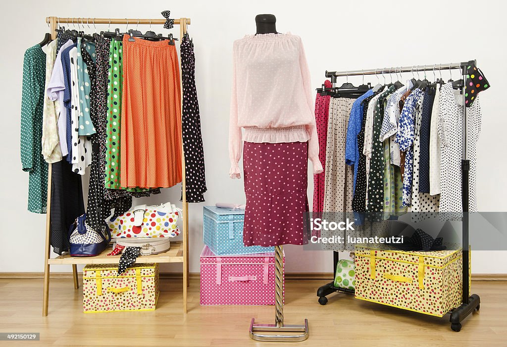 Dressing closet with polka dots clothes arranged on hangers. Colorful wardrobe with polka dots clothes, a pink outfit on a mannequin and accessories. Arranging Stock Photo