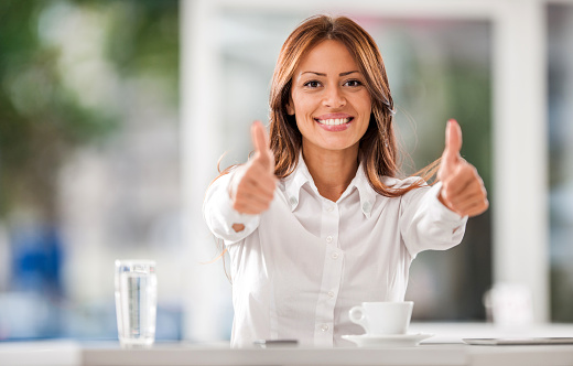 Happy businesswoman showing thumbs up while sitting in a cafe and looking at camera.