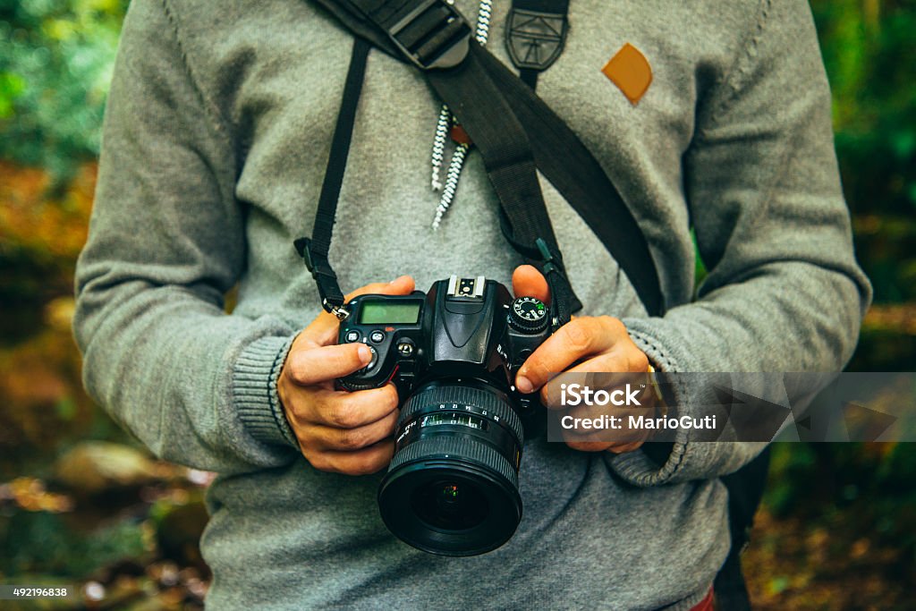 Young man holding camera A young man holding a DLSR camera in a natural environment. 2015 Stock Photo