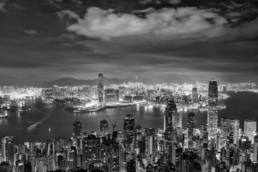 This is a horizontal, black and white photograph at night of Hong Kong viewed from Victoria Peak. Grainy with high ISO.