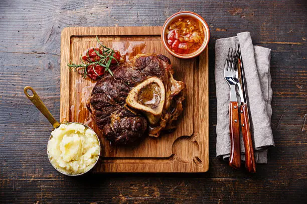 Prepared Osso buco Veal shank with tomatoes and mashed potatoes on serving board on wooden background