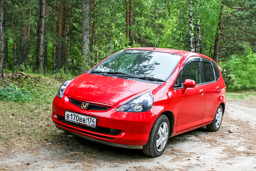 Miass, Russia - June 12, 2009: Red compact motor car Honda Fit is parked in the forest.