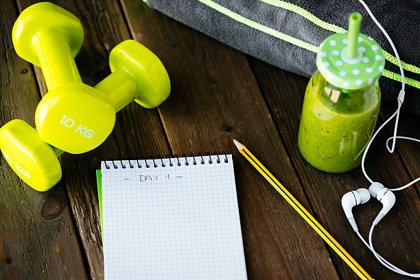 Fitness workout routine blank notebook and detox smoothie Blank copy space workout routine notebook, detox green smoothie, dumbbells and earphones on wooden table for dieting and healthy fitness nutrition concept.  Diet and training planning. exercise routine stock pictures, royalty-free photos & images