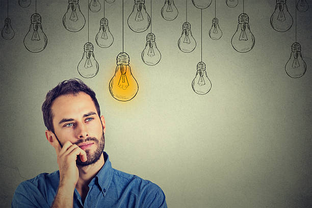 man looking up with idea light bulb above head Portrait thinking handsome man looking up with idea light bulb above head isolated on gray wall background man with a light bulb over his head stock pictures, royalty-free photos & images
