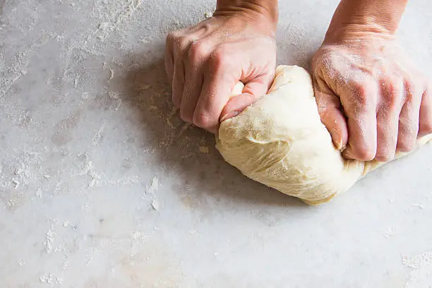 Hands kneading dough on white table