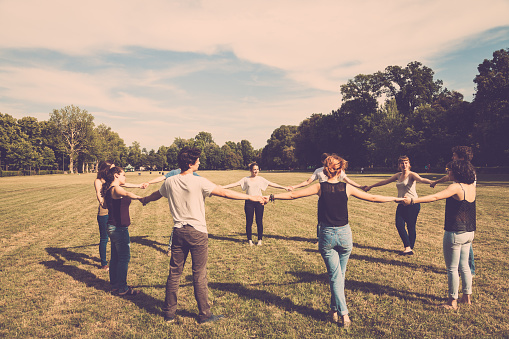 Group of teenagers in a park holding hands in circle.