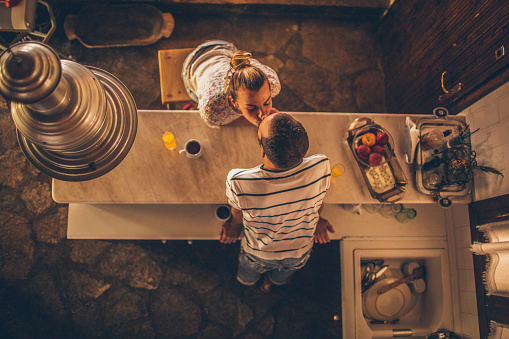 Loving couple is having their first cup of coffee and a kiss in their rustic kitchen; high angle view