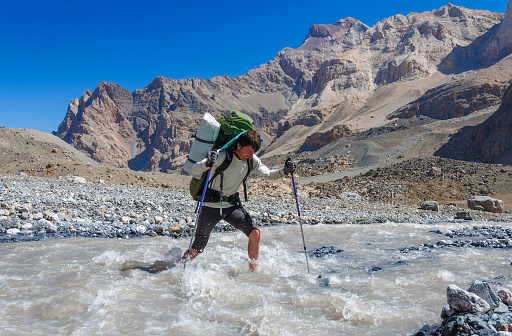 Hiker crossing mountain river. Fany mountain. Tadjikistan