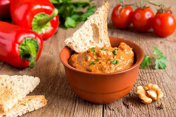 roasted pepper dip with nuts and bread in ceramic bowl over rustic wooden background closeup