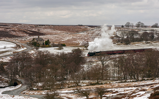 Goathland, Yorkshire, UK. Vintage steam train under full steam makes its way from Goathland to Pickering through the North York Moors covered in snow in winter near Goathland, Yorkshire, UK.