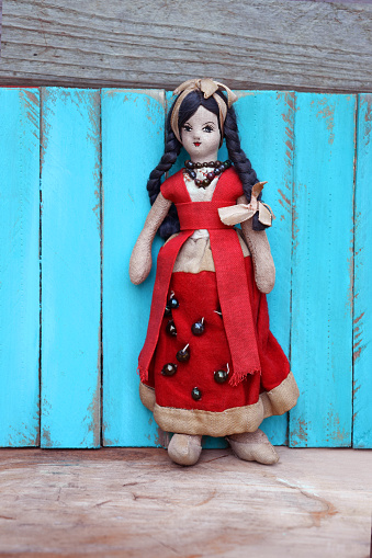This is a picture of a vintage Mexican cloth girl doll in a red dress and bow in her hair. The doll is against an aqua blue wood background on a wood floor.