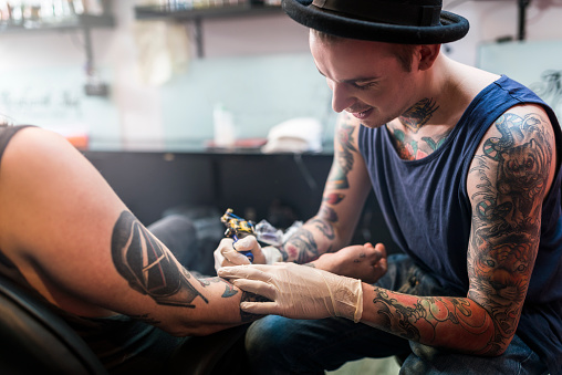 A photo of artist making tattoo on male customer's hand. Tattoo expert is working in studio. Cropped image of man getting his hand tattooed.