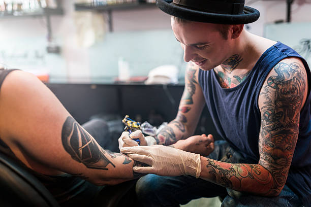 artist making tattoo on male customer's hand in studio - dövme yaptırmak fotoğraflar stok fotoğraflar ve resimler