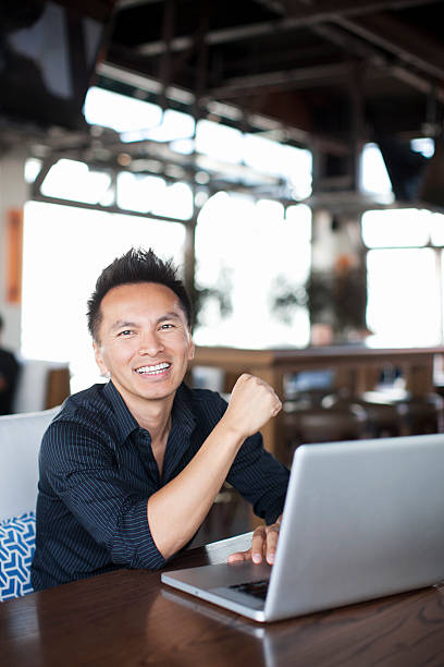 istock Smiling Asian male sitting in front of laptop computer 492259164