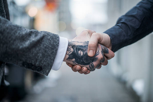 Tattooed businessman greeting colleague outdoors A photo of business people shaking hands outdoors. Cropped image of tattooed businessman greeting female colleague. Male executive is with animal and text tattoo on hand. animal representation photos stock pictures, royalty-free photos & images