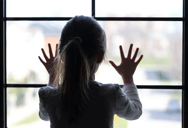 Young girl at window (in partial silhouette) hands pressed against window, pensive or wanting out?