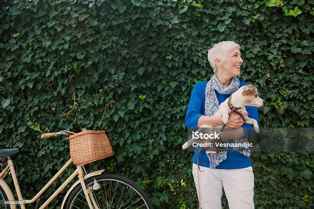 Woman with dog Beautiful mature woman holding dog, leaves behind them and bicycle Senior Adult Stock Photo
