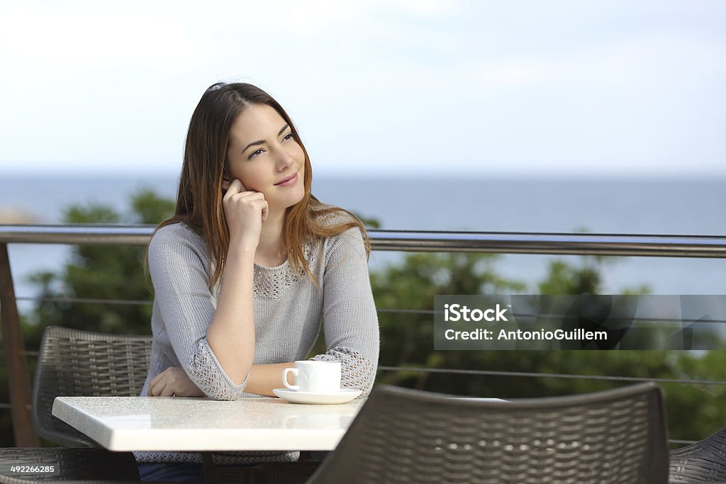 Woman pensive sitting in a terrace of a restaurant Dreamer woman pensive sitting in a terrace of a restaurant with the beach in the background Adult Stock Photo