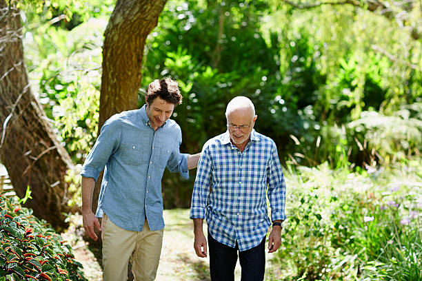 senior man and son walking in park - senior adult stock-fotos und bilder