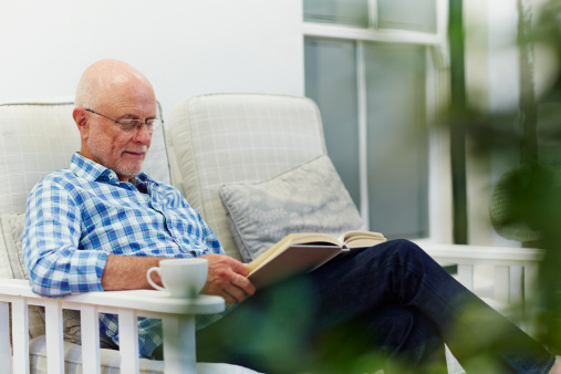 Stylish mature man reading book after hard working day while sitting on cosy sofa. Domestic lifestyle concept