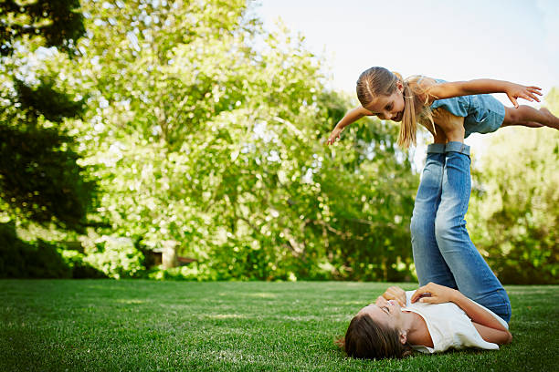 mother lifting daughter with legs in park - playful mother playing daughter стоковые фото и изображения