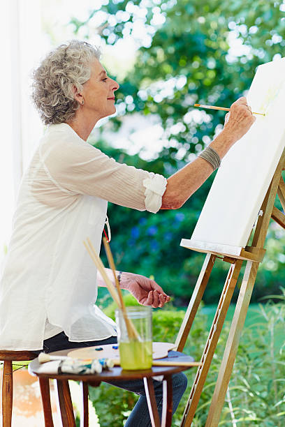 senior woman painting in park - easel adult art creativity stock-fotos und bilder
