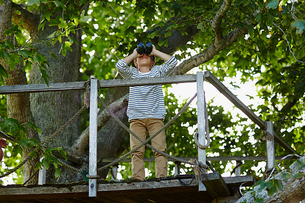 boy using binoculars on treehouse - children only tree area exploration freshness fotografías e imágenes de stock