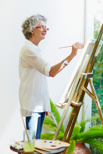 Side view of senior woman painting on canvas at porch