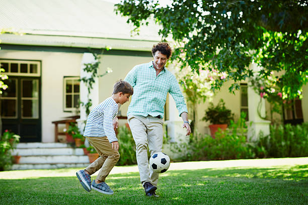 father and son playing soccer in lawn - adult activity child father stock-fotos und bilder