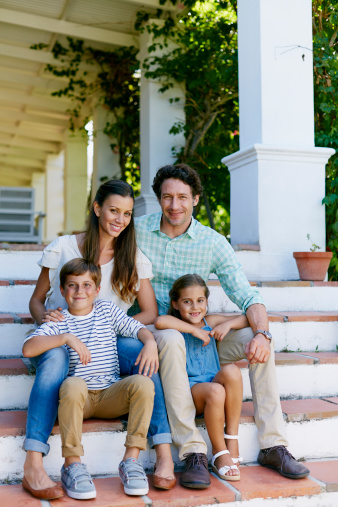 Full length portrait of happy parents with children sitting on steps outside home