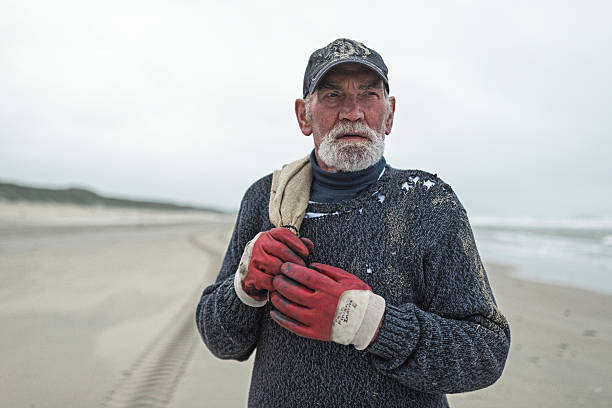 istock Senior beachcomber with work gloves on the beach holding sack. 492277238
