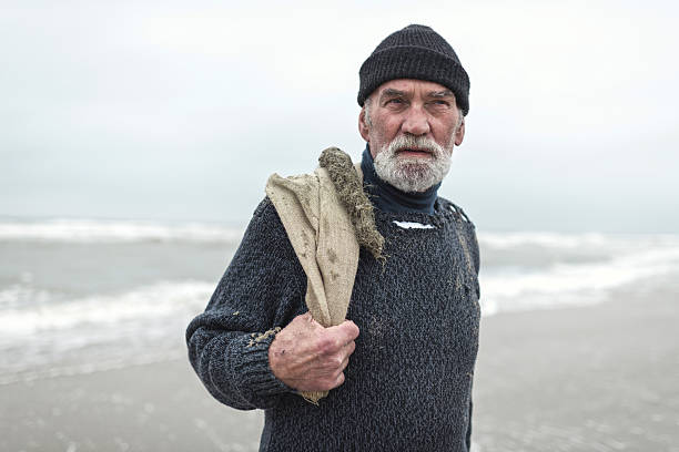 istock Senior beachcomber with burlap sack and woolen cap near sea. 492277414
