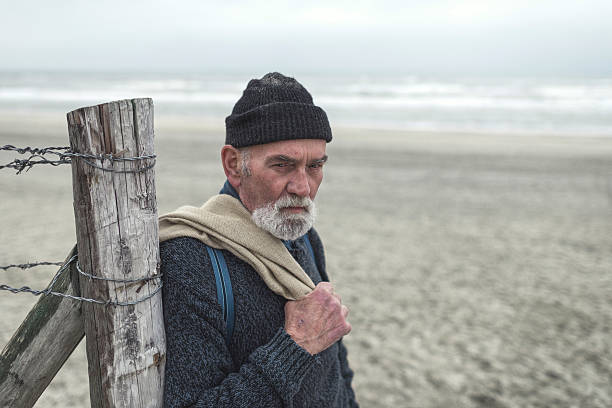 istock Serious beachcomber on the beach leaning against wooden post fence. 492277440