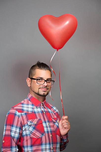 istock Handsome hipster man with red heart baloon in studio 492279542