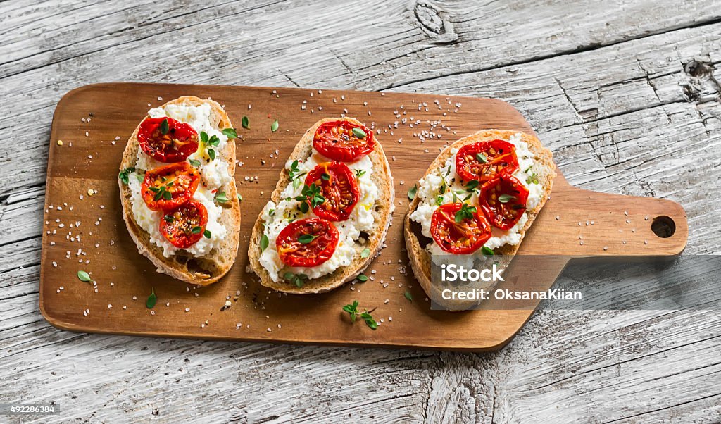 sandwich with goat cheese, sun-dried tomatoes and thyme sandwich with goat cheese, sun-dried tomatoes and thyme, served on the Board at a bright wooden surface Bruschetta Stock Photo