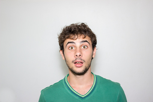 Portrait of shocked excited worried young man raised his arms, looking at camera, sees something unbelievable, saying wow, wearing blue shirt. Indoor studio shot isolated on gray background.