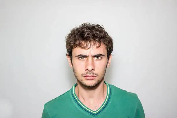 Portrait of furious young man against gray background. Furious teenage boy standing in front of gray background and looking at camera with furious facial expression. Image taken in studio and developed from Raw format.