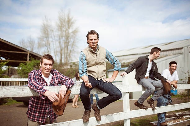 Group of cowboy friends hanging out, sitting on fence, having a good time laughing.