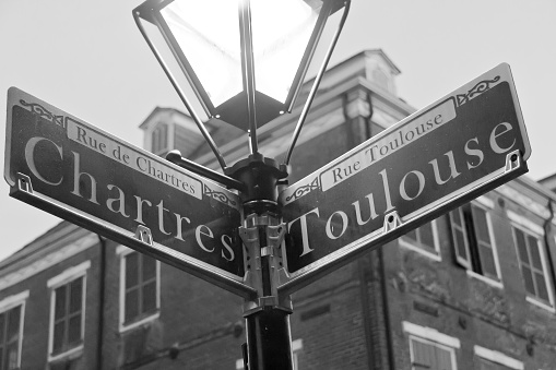 A black and white photo of the street name signs at the Chartres and Toulouse streets intersection in the French Quarter of New Orleans. 