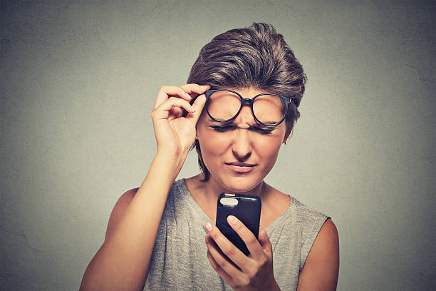mujer joven con gafas teniendo problemas para ver teléfono celular - entrecerrar los ojos fotografías e imágenes de stock