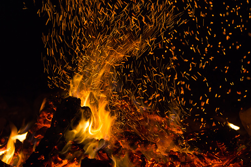A bonfire with lots of sparks shooting up from the fire at night.