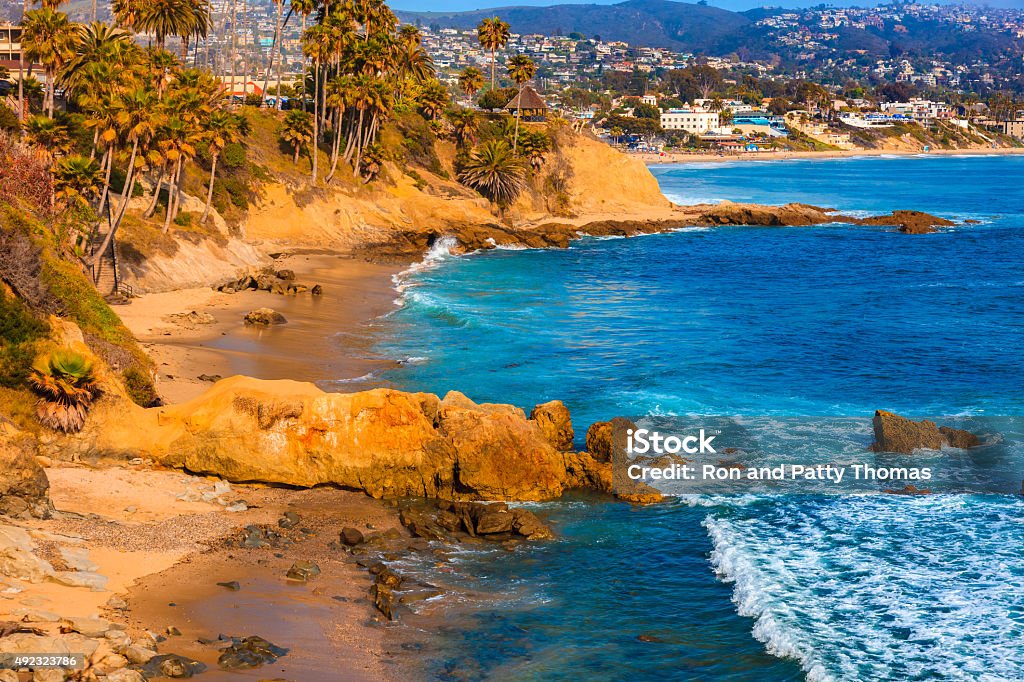 Laguna Beach coastline,Pacific Ocean,Rte 1,Orange County,CA Rocky cliffs with palm trees fill the leftside foreground leading back to beach and breaking surf of Laguna Beach and city with hillside houses, California California Stock Photo