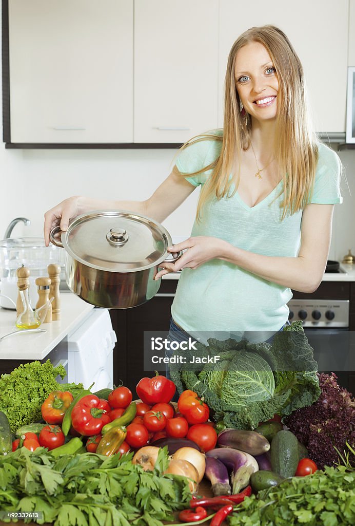 happy blonde woman  with pan and vegetables happy blonde woman  with pan and heap of fresh vegetables in kitchen 20-24 Years Stock Photo