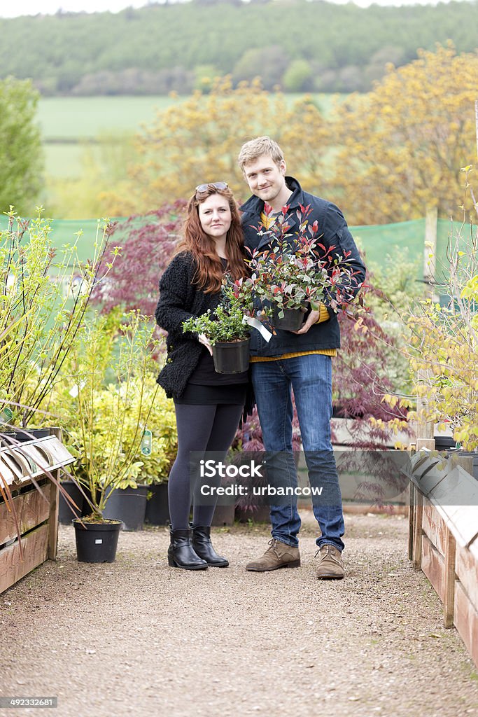 Garden centre choice A couple hold a shrub each, whilst looking directly at the camera,  in a Devon garden centre. Sidmouth Garden Centre, Sidmouth, Devon.   Adults Only Stock Photo