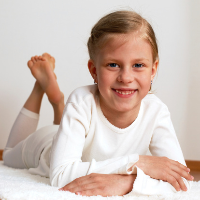 Little blonde girl is lying on the white carpet in the room