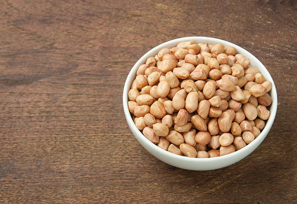 istock Raw peanuts in white bowl on wooden table. 492361648