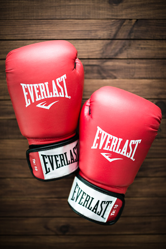 Florence, Italy - September 29, 2015: Close up of red Everlast boxing gloves apparel on a plank table Everlast is one of the most famous brand for boxing sport. Studio shot.