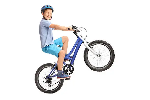 Joyful little boy performing a wheelie with his bike and looking at the camera isolated on white background